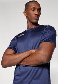 T-shirt atlético azul-marinho feito de um tecido suave e leve. Apresenta mangas curtas e um decote arredondado, com um logótipo discreto no peito.