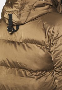 Chaqueta marrón acolchada con un acabado brillante, que presenta una capucha y detalles de tiras negras. Textura suave con secciones acolchadas para aislamiento.