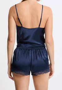 Camisole en satin marine avec bretelles ajustables, associé à un short assorti avec des finitions en dentelle au bas. Texture lisse sur l'ensemble.