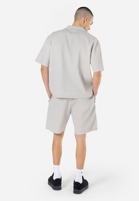 Light gray short-sleeve shirt and matching shorts made of ribbed fabric. Features relaxed fit, two side pockets, and dark sneakers.