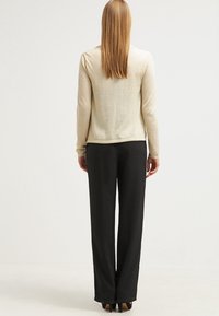 Ljus beige långärmad topp i strukturerad stickning, kombinerad med svarta vida byxor. Outfiten har en enkel, minimalistisk design.