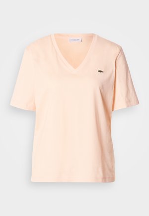 Halvány őszibarack színű, pamutból készült V-nyakú rövid ujjú póló, melyen a bal mellrészen egy kis zöld Lacoste logó található.