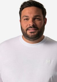 Hvid bomulds t-shirt med rund hals og korte ærmer, prydet med et lille, lysfarvet "M" logo på venstre brystområde.