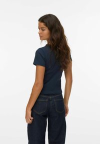 Marineblå, tætsiddende kortærmet t-shirt lavet af bomuld, parret med højtaljede mørke denim jeans med baglommer og syninger.