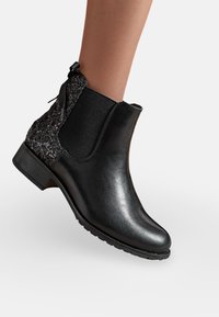Bottines en cuir noir avec une finition lisse, panneau latéral élastique et talon texturé pailleté. Talon bloc bas et semelle en caoutchouc pour une meilleure adhérence.