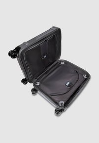 Valise noire à roulettes avec coque rigide, compartiments zippés et poche intérieure en filet. Dispose de roues pivotantes à 360 degrés et de poignées robustes.