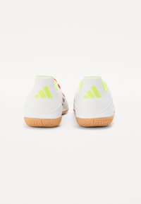 Scarpe da ginnastica bianche con dettagli verde neon, dotate di una suola in gomma strutturata e tre strisce diagonali sul tallone.