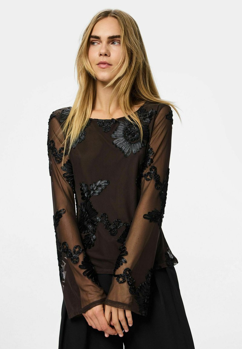 Mustast läbipaistvast materjalist pika varrukaga pluus, millel on keerukad tikitud lillemustrid. Pehme tekstuur, voolav lõige ja ümar kaelus.