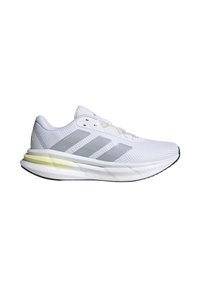 Zapatilla deportiva blanca con parte superior de malla, diseño de tres rayas grises, suela acolchada y acento amarillo claro en el talón, con cierre de cordones.