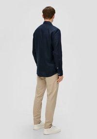 Camicia a maniche lunghe blu navy in tessuto leggero, con polsini abbottonati, abbinata a pantaloni beige e sneakers bianche. Vista posteriore mostrata.