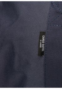 Stor navy blå cargo duffel taske i tekstureret stof, med et sort mærke der står "CARGO DUFFEL XLARGE."