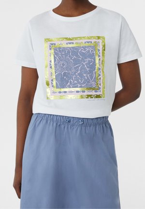 White short-sleeve cropped shirt with blue and gold floral square print, worn with light blue elastic waist skirt with buttons.