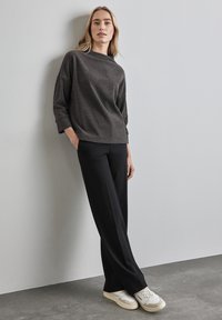 Dunkelgrauer strukturierter Pullover mit weitem Ausschnitt, kombiniert mit schwarzen lockeren Hosen und hellen Sneakers vor einem grauen Hintergrund.