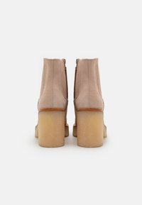 Botas de tobillo de ante beige con tacón cuadrado y cierre de cremallera en la parte trasera. Textura suave con detalles de costura expuesta y suela resistente.