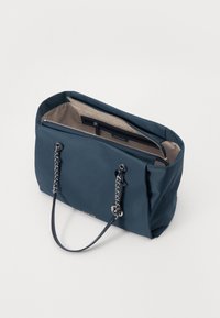 Sac fourre-tout bleu marine avec une texture lisse, une fermeture à glissière et des anses ornées de chaînes argentées. L'intérieur est doté d'une doublure beige clair.