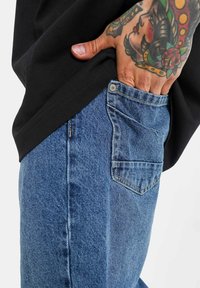 Blå denimjeans med en lätt blekning, med en klassisk passform, detaljerad stickning på bakfickorna och en silverknapp vid midjan.