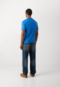 T-shirt de algodão azul com mangas curtas e decote redondo, combinada com jeans de perna reta azul claro e sapatos slip-on em tom bege.