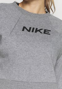 Ripresa ravvicinata di una persona che indossa una felpa grigia con il testo "NIKE" nero centrato sul petto.