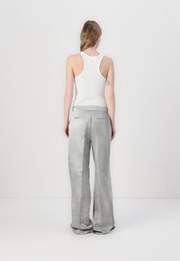 Lys grå, vide bukser med en glat tekstur og baglommer, sammen med en hvid ribbet tanktop, sett fra baksiden.