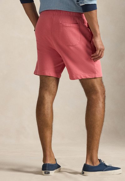 Ροζ βαμβακερά σορτς με ελαστική μέση και πλαϊνές τσέπες. Διαθέτουν μία πίσω τσέπη. Φοριούνται με μπλε καμβά παπούτσια.