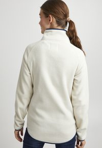 Valgest fleece-pullover, millel on kõrge krae, sinine ääreäär, tekstureeritud pind ja lõdvestatud istuvus. Tagakülje vaade näitab õmblusi õlgadel.