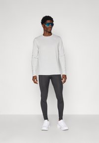 Maglietta sportiva a maniche lunghe grigia chiara, leggings neri aderenti e sneaker bianche. Il personaggio indossa grandi occhiali da sole blu.