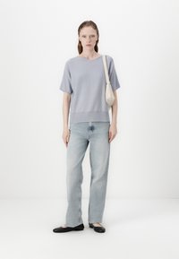 Lys blå kortermet genser med V-hals, kombinert med lyse denimjeans. Modell iført svarte balletleiligheter og holder en liten beige veske.