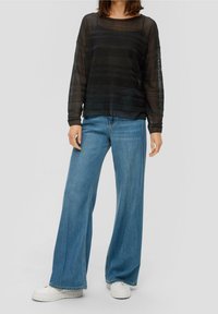 Haut noir transparent à manches longues avec rayures horizontales, associé à un jean large bleu clair et des baskets blanches à plateforme.