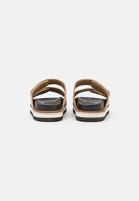 Brune sandaler med et dobbeltrem-design, der har en sort fodseng og en hvid og sort stribet sål. Flad, afslappet stil, åndbart materiale.