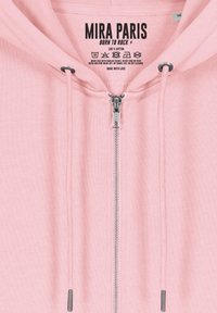 Felpa di cotone rosa con zip completa e cappuccio con cordini. Presenta accessori in metallo argentato, un tessuto testurizzato e un'etichetta stampata all'interno.