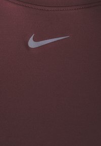 Μπορντό αθλητικό tank top με λεία υφή, διαθέτει ασημί λογότυπο Nike στο κέντρο του στήθους. Σχεδίαση racerback με ελάχιστη ραφή.