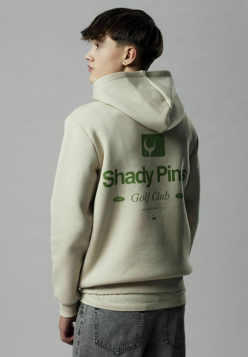 Bež dukserica s velikim zelenim grafičkim motivom na leđima koji prikazuje tenisku oznaku i natpis "Shady Pins Golf Club", rebrasti manžeti i kapuljača s vezicom.