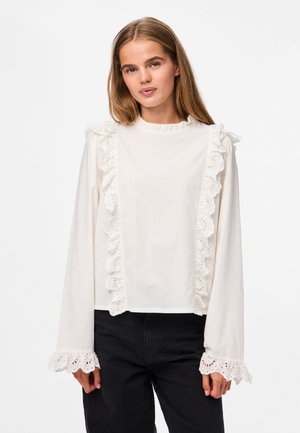 Haut blanc à manches longues avec une bordure en dentelle à œillets sur le devant et les manches, tissu texturé et encolure ronde. Coupe décontractée.
