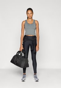 Γκρι τοπ και μαύροι ψηλόμεσοι κολάν, κρατώντας μια μαύρη σάκα duffel. Γκρι αθλητικά παπούτσια ολοκληρώνουν την εμφάνιση. Απλός, λειτουργικός σχεδιασμός.