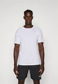 Hvit atletisk t-skjorte med korte ermer, rund hals og subtil merking. Brukt sammen med svarte shorts med en logo. Glatt tekstur.