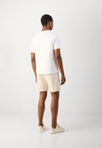 Witte t-shirt met korte mouwen en een rechte zoom, gecombineerd met beige shorts. Schoeisel is lichtgekleurde sneakers. Minimalistisch ontwerp, zachte textuur.
