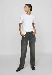 Hvit t-skjorte med rund hals, kombinert med høyt liv og løse, mørkegrå jeans. Merker som er verdt å nevne inkluderer synlige sømmer og oppbrettede kanter.