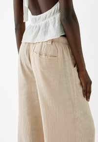 Lichtbeige wijde broek met een zachte textuur, voorzien van een elastische tailleband en een enkele achterzak.