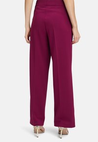 Wijdvallende broeken van een diepe magenta stof, met een soepele textuur en een hoge taille. Afgewerkt met neutrale sandaaltjes met banden.