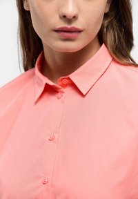 Coral button-up shirt with a spread collar, featuring smooth fabric, five matching buttons, and clean stitching details.