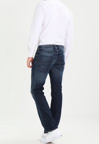 Mörkblå denimjeans med rak passform, fem fickor och klassisk design, ihop med en vit långärmad skjorta och vita sneakers.