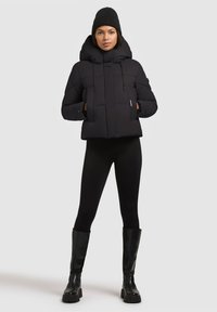 Sort dunjakke med høj krave, der har vandrette stikninger, snor i hætten og sidelommer, parret med sorte leggings og blanke knæhøje støvler.