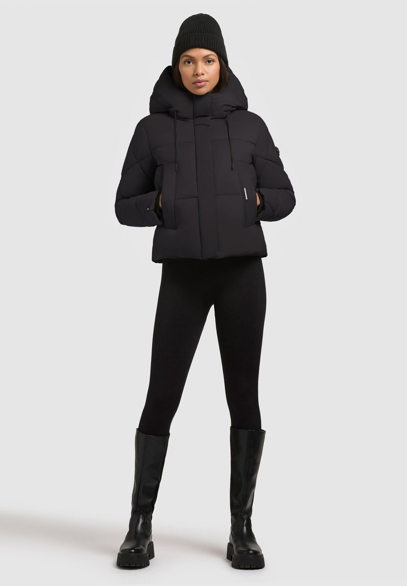 Sort dunjakke med høj krave, der har vandrette stikninger, snor i hætten og sidelommer, parret med sorte leggings og blanke knæhøje støvler.