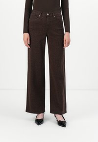 Braun gepunktete, weit geschnittene Jeans mit hoher Taille, ausgestattet mit fünf Taschen und silberfarbener Hardware, kombiniert mit schwarzen spitz zulaufenden Ballerinas.