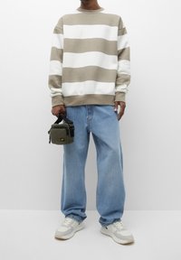 Pull rayé beige et blanc, jeans baggy bleu clair, tenant un petit sac vert olive avec une sangle noire. Tennis blanches avec des accents beiges.
