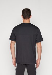 Černé krátké tričko s hladkým materiálem, s jednobarevným zadním designem a jemnými vertikálními švy pro přidaný detal.