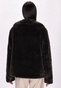 Giacca in pelliccia sintetica marrone scuro con vestibilità rilassata, spalle basse e maniche ampie. Tessuto morbido con colletto e senza chiusure visibili.