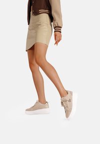 Sneakers beige con una toma a trama, accenti in pelle liscia e una suola platform bianca. Presentano cuciture decorative e un dettaglio con il logo.