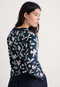 Sötétkék pulóver fehér virágmintával. Kerek nyakkivágással és bordázott mandzsettával rendelkezik. Puha pamut anyag, laza fazon és könnyű textúra.