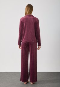 Burgundy loungewear-sæt med en langærmet top med krave og brede bukser, lavet af blødt, luksuriøst stof.
